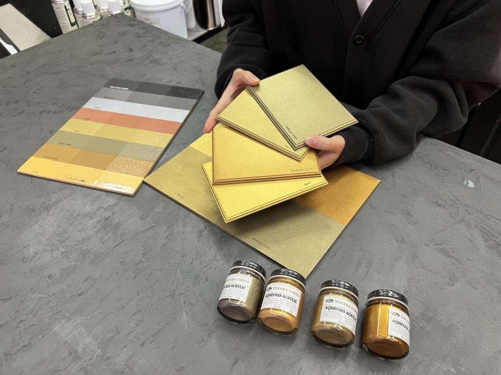 ゴールド系塗料の仕上がりを、見本板で実際に比較確認している場面
